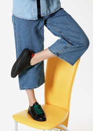 Woman in stylish shoes standing on chair against white background, closeup