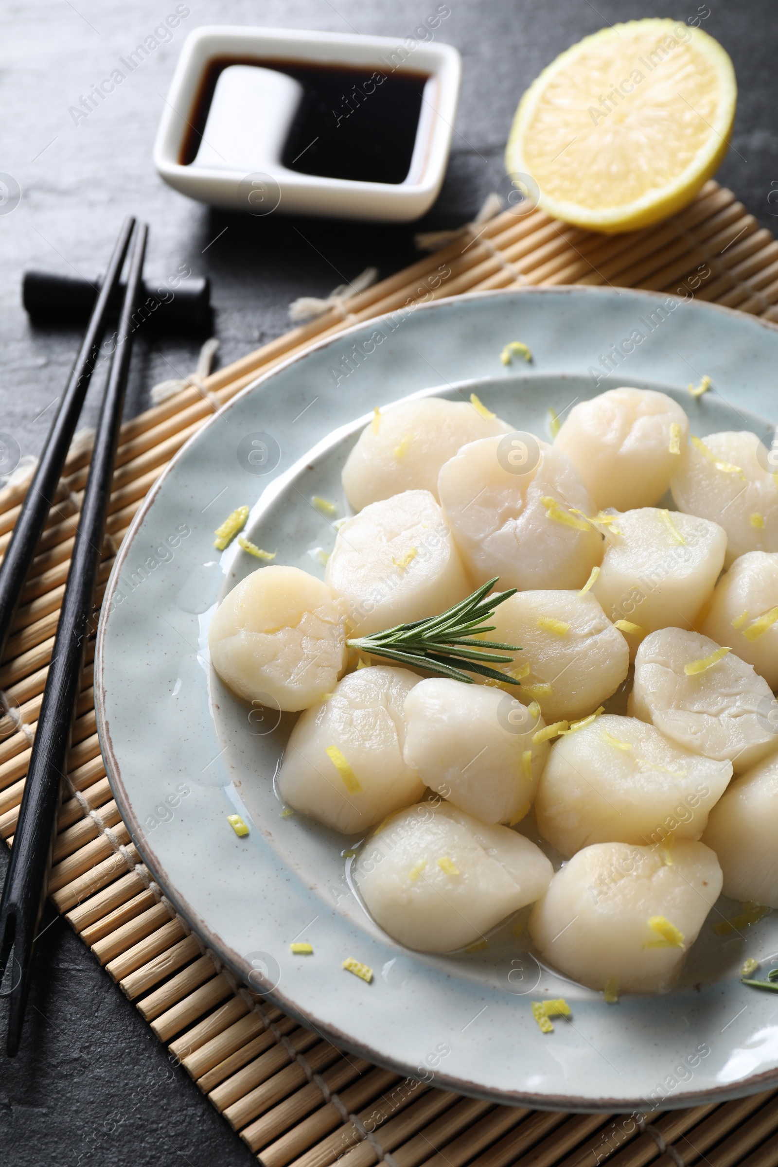Photo of Raw scallops with lemon, rosemary and soy sauce on dark textured table, closeup