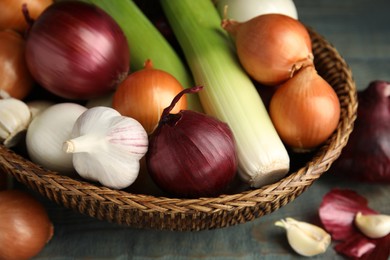 Photo of Wicker basket with fresh onion bulbs, leeks and garlic on light blue wooden table, closeup