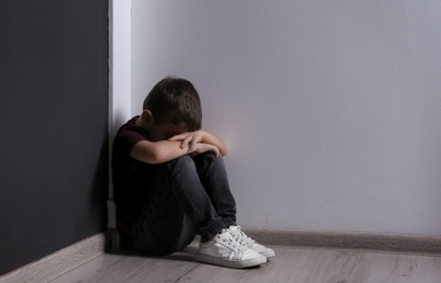 Photo of Sad little boy sitting on floor indoors. Space for text