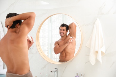 Handsome young man applying deodorant in bathroom