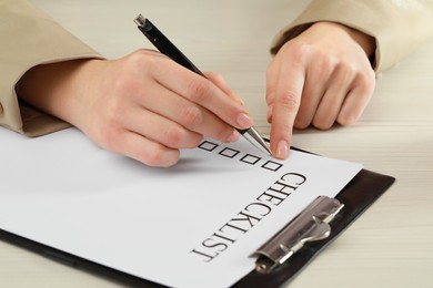 Photo of Woman filling Checklist at white wooden table, closeup