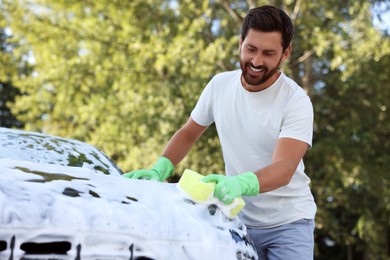 Happy man washing car with sponge outdoors