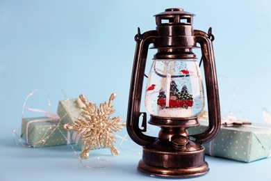 Beautiful Christmas snow globe in vintage lantern, gift box and festive decor on light blue background