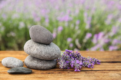 Photo of Spa stones and fresh lavender flowers on wooden table outdoors, closeup. Space for text