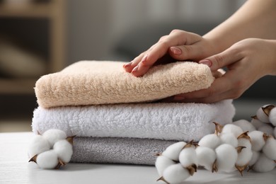 Photo of Woman taking terry towel and cotton flowers on white wooden table in room, closeup