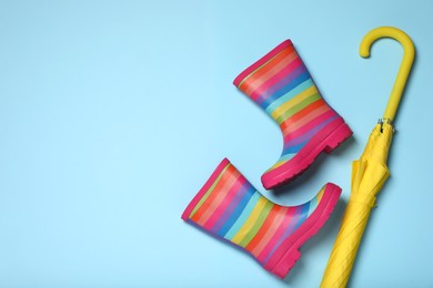 Photo of Striped rubber boots and yellow umbrella on light blue background, flat lay. Space for text