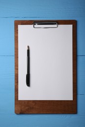 Photo of Clipboard with sheet of paper and pen on light blue wooden table, top view. Space for text