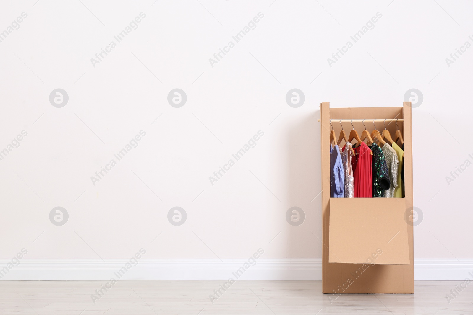 Photo of Wardrobe box with clothes against light wall indoors. Space for text