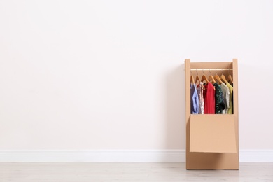 Photo of Wardrobe box with clothes against light wall indoors. Space for text