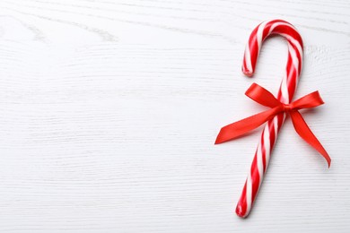 Photo of Sweet Christmas candy cane with bow on white wooden table, top view. Space for text