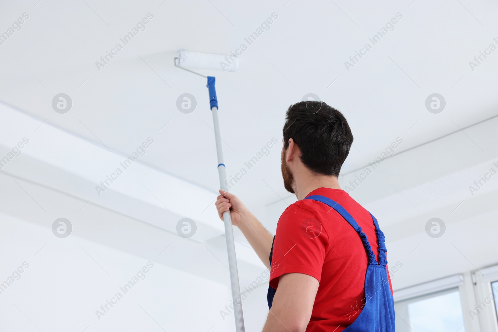 Photo of Handyman painting ceiling with roller in room, back view