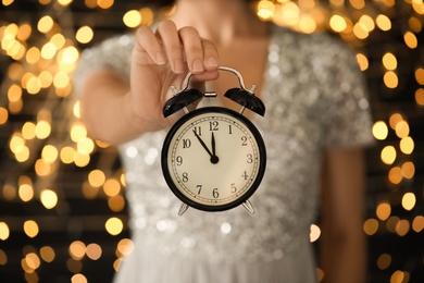 Photo of Woman holding alarm clock against blurred lights, closeup. New Year countdown