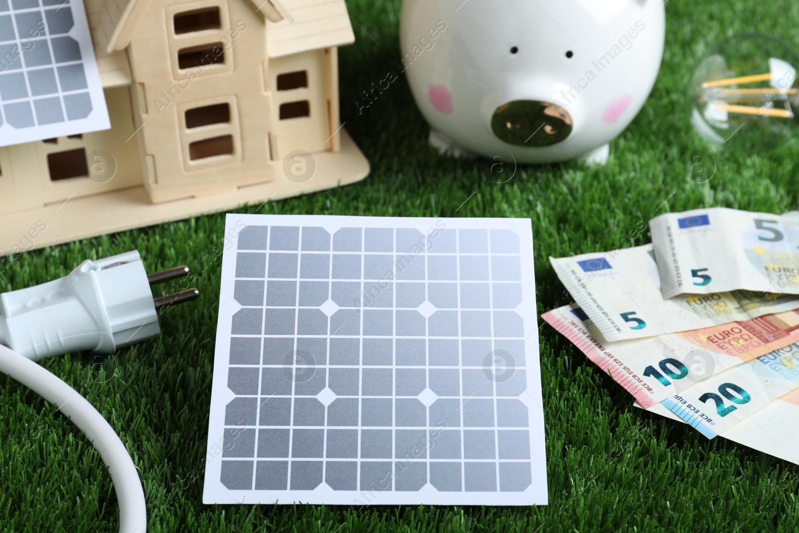 Photo of Solar panels, house model and money on green grass, closeup