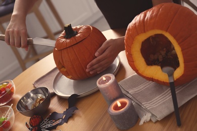 Photo of Woman making pumpkin jack o'lantern at wooden table, closeup. Halloween celebration