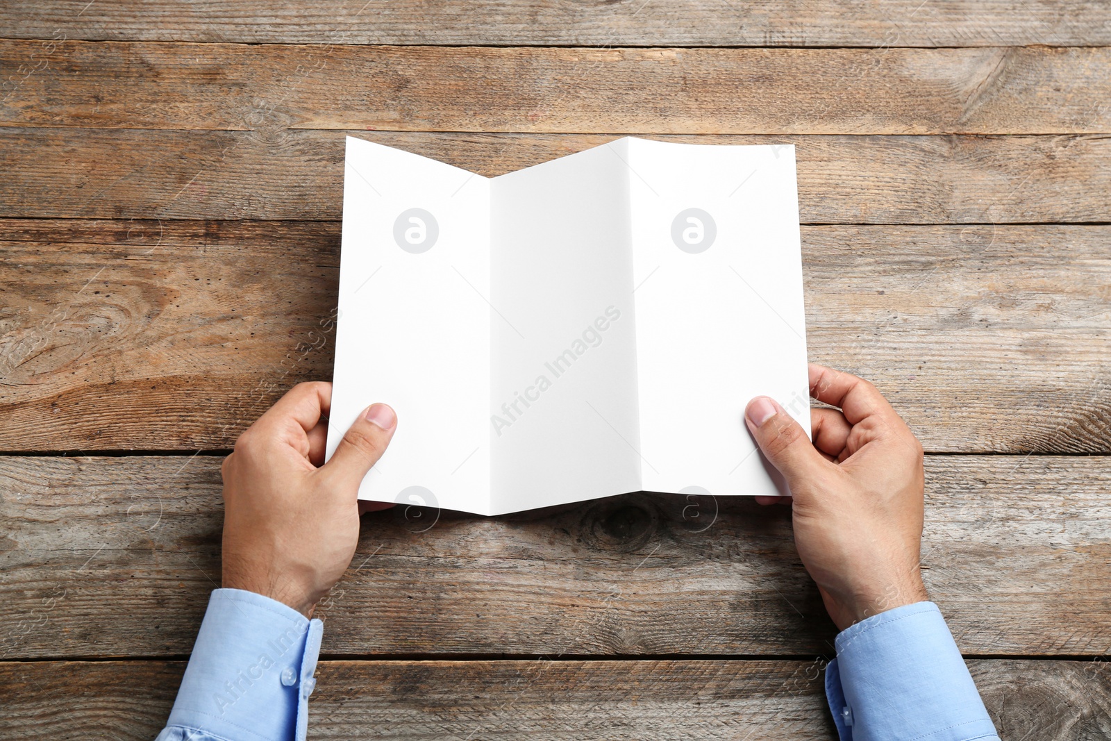 Photo of Young man holding blank brochure at wooden table, top view. Mock up for design