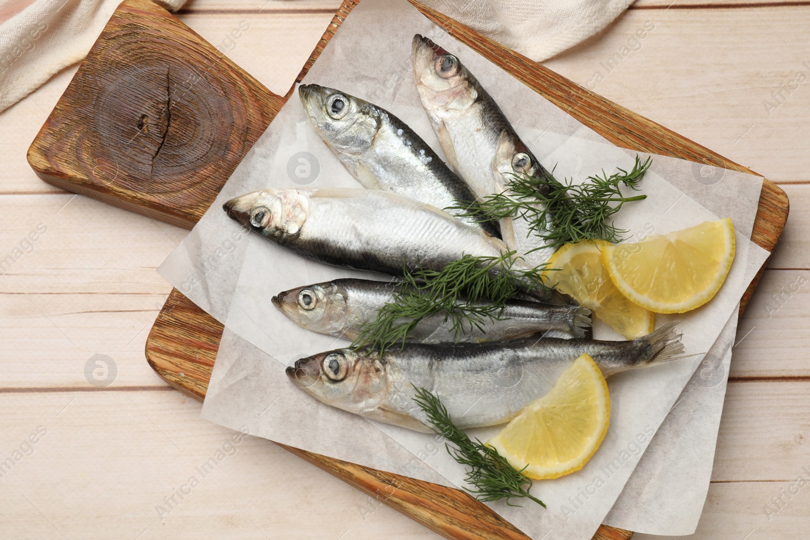 Photo of Fresh raw sprats, lemon and dill on light wooden table, top view