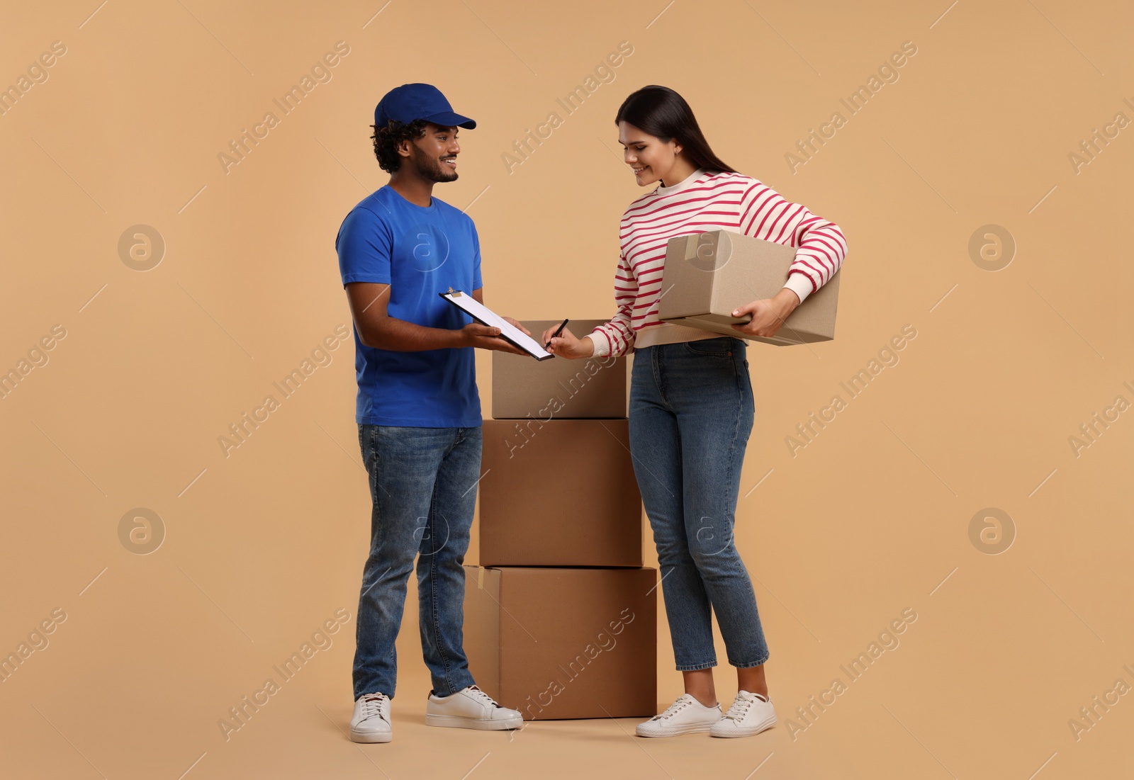 Photo of Smiling woman signing order receipt on light brown background. Courier delivery