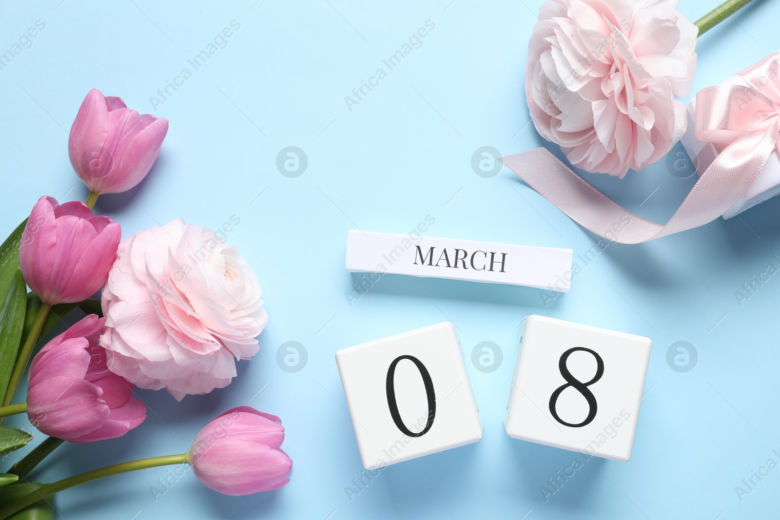 Photo of International Women's day - 8th of March. Gift box, wooden block calendar and beautiful flowers on light blue background, flat lay