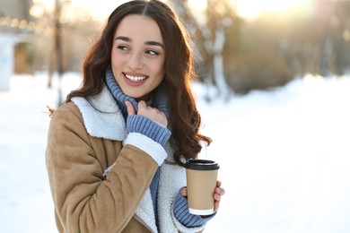 Photo of Portrait of smiling woman with paper cup of coffee in snowy park. Space for text