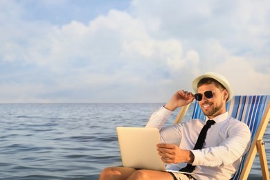 Happy man with laptop on deckchair near sea. Business trip