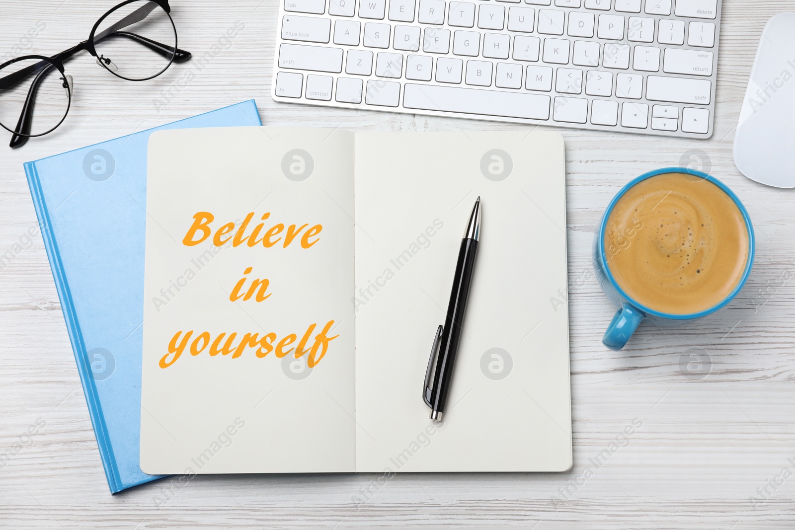 Image of Phrase Believe in Yourself in notebook, computer keyboard and cup of coffee on white wooden desk, flat lay