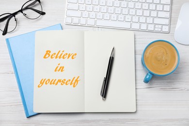 Phrase Believe in Yourself in notebook, computer keyboard and cup of coffee on white wooden desk, flat lay