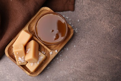 Photo of Yummy caramel candies, sauce and sea salt on brown table, top view. Space for text