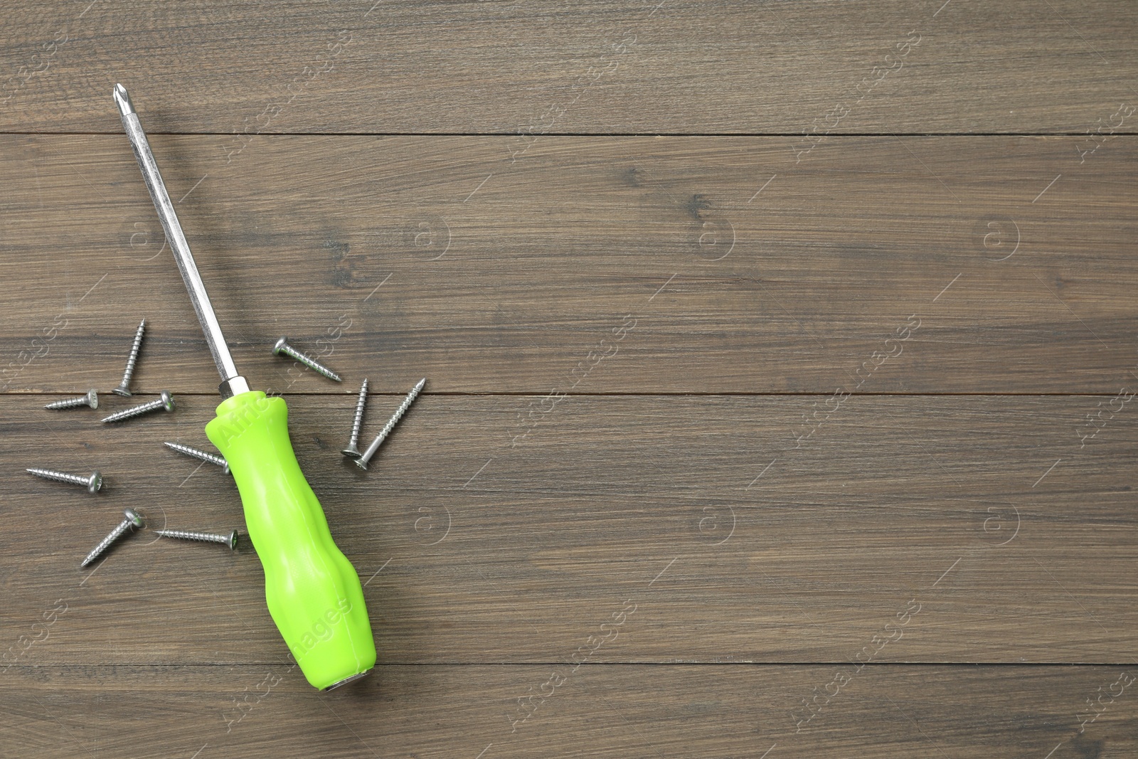 Photo of Screwdriver with green handle and screws on wooden table, flat lay. Space for text