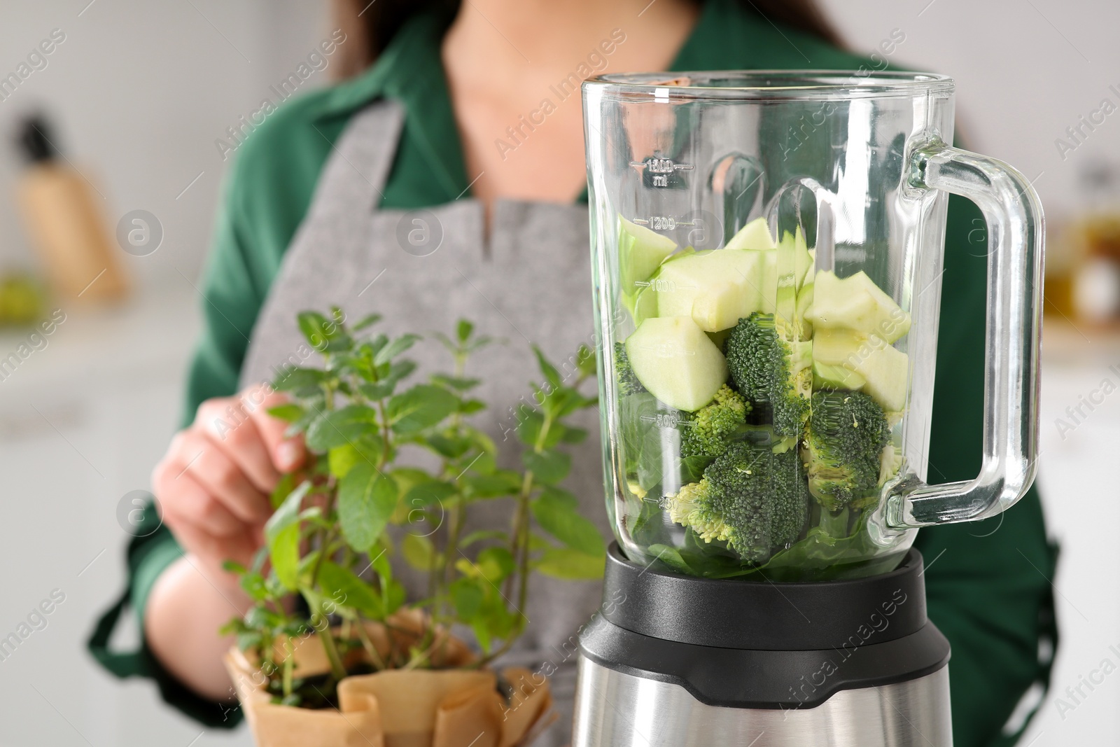 Photo of Woman holding potted herb indoors, focus on blender with ingredients for smoothie