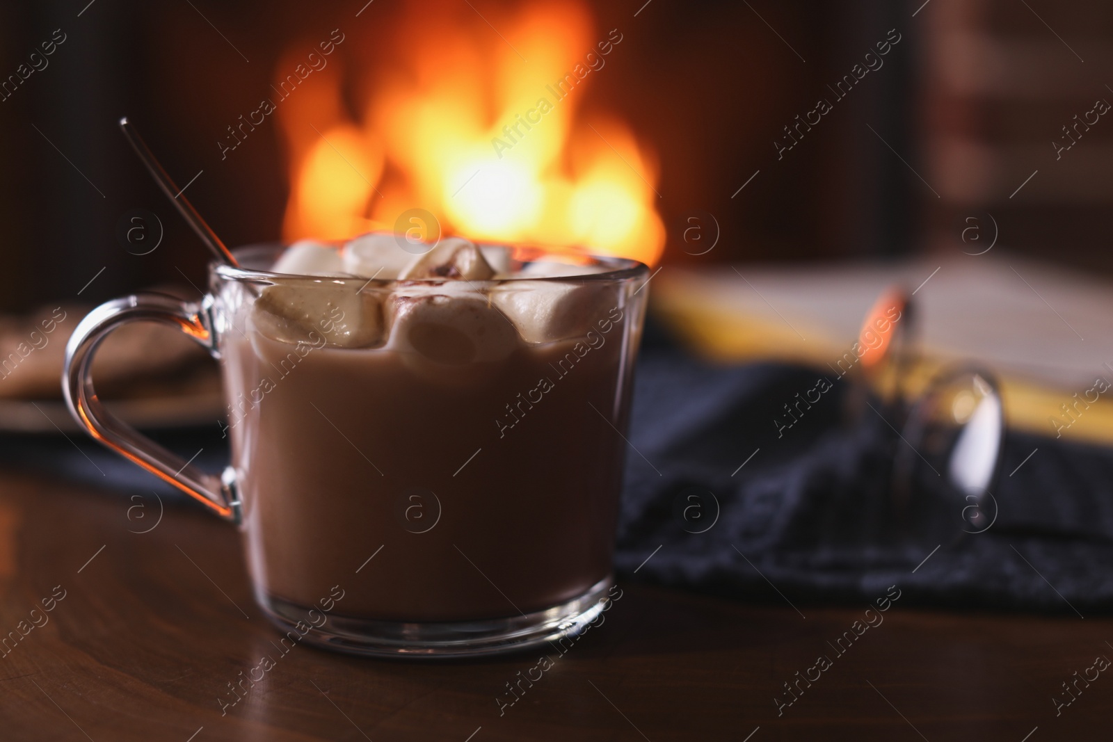 Photo of Delicious sweet cocoa with marshmallows and blurred fireplace on background