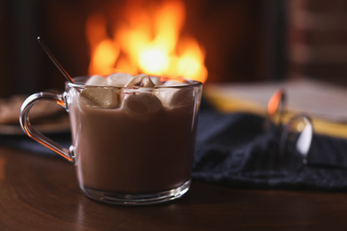 Photo of Delicious sweet cocoa with marshmallows and blurred fireplace on background