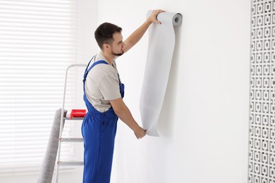 Man hanging stylish gray wallpaper in room