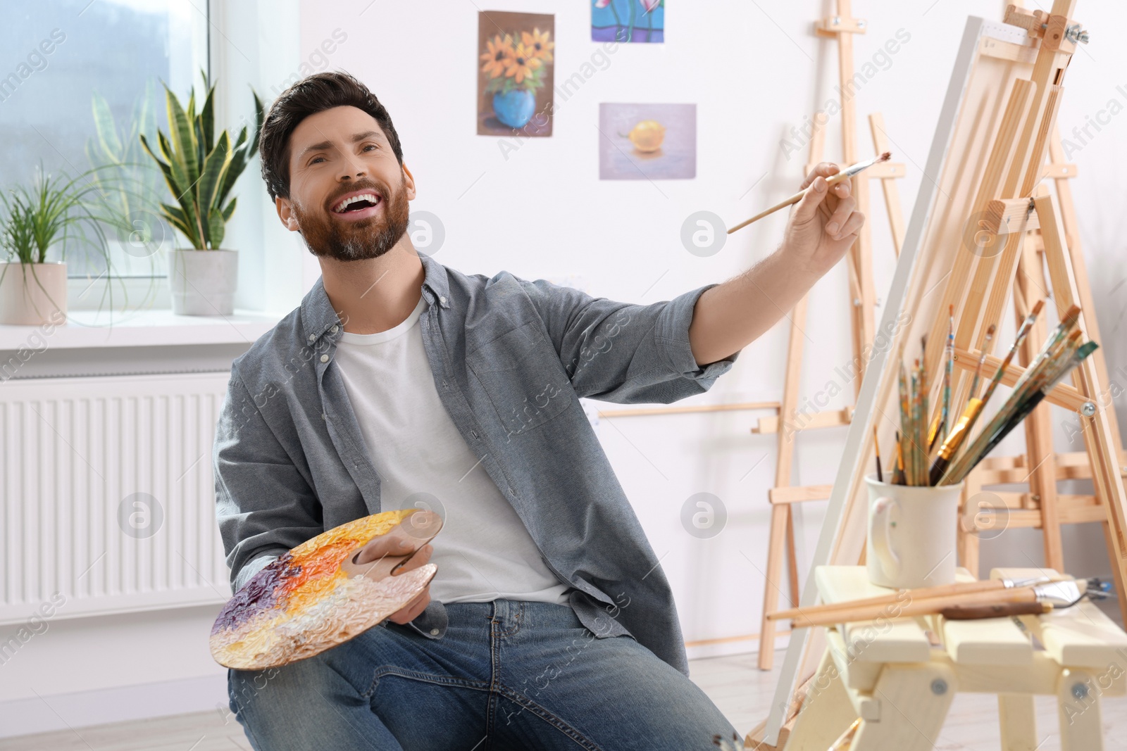 Photo of Happy man painting in studio. Using easel to hold canvas