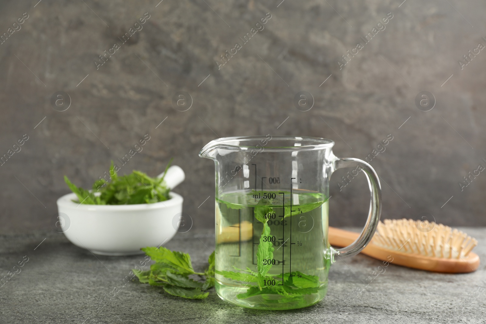 Photo of Stinging nettle extract and brush on grey background. Natural hair care