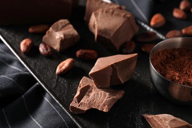 Photo of Pieces of tasty milk chocolate, cocoa beans and powder on table, closeup