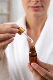 Woman with bottle of cosmetic serum and dropper on blurred background, closeup