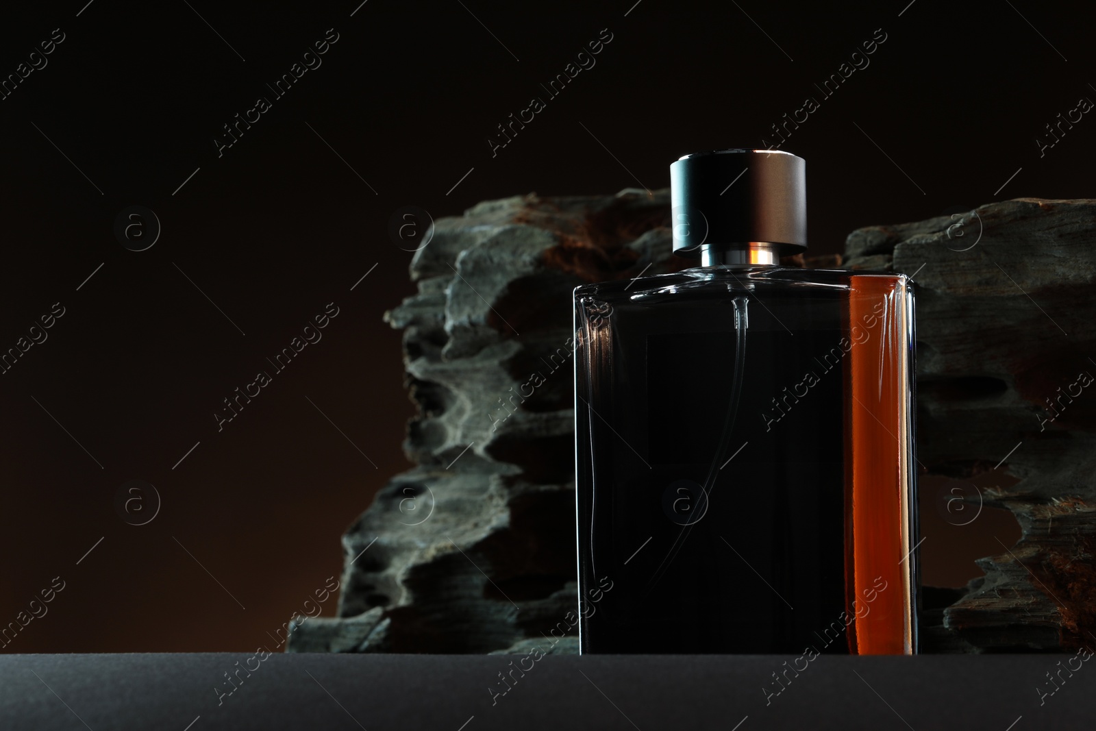 Photo of Luxury men`s perfume in bottle on grey table against dark background, space for text