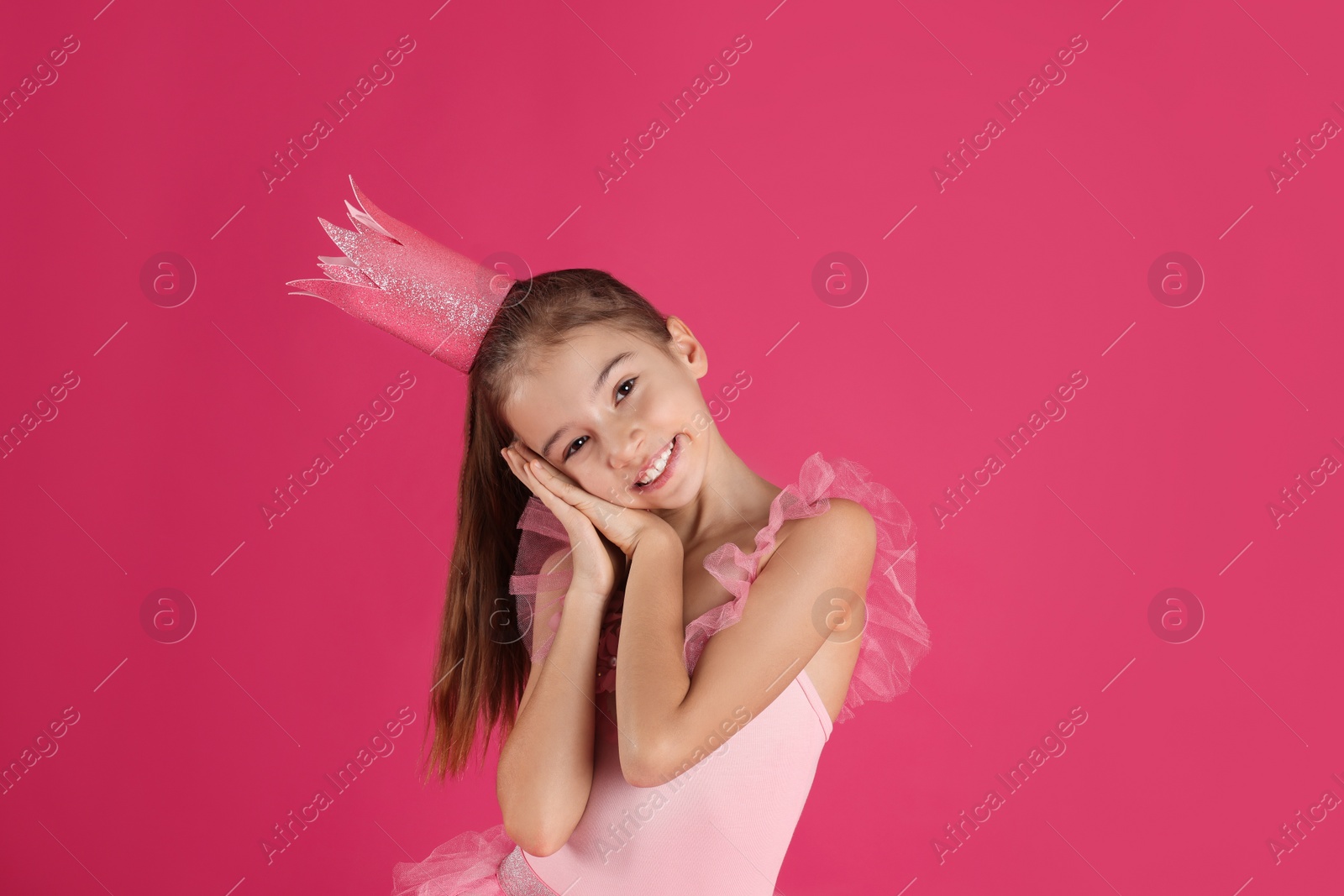 Photo of Cute girl in beautiful dress with crown on pink background. Little princess