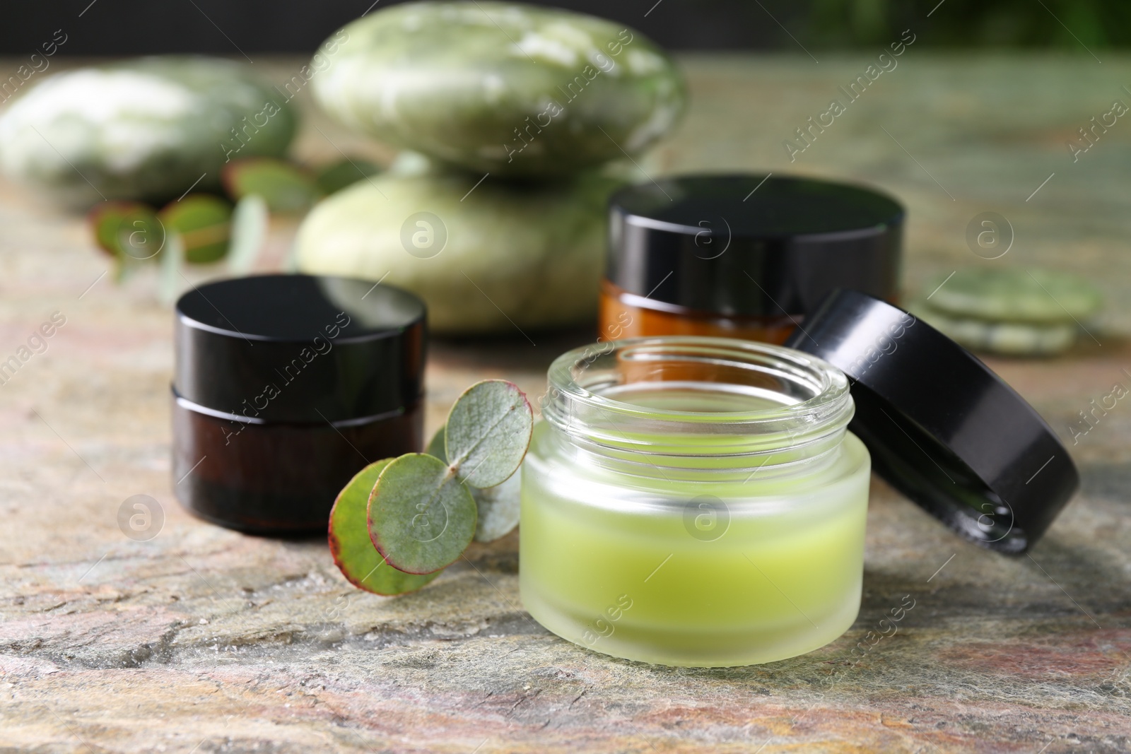 Photo of Jars of cream and eucalyptus leaves on textured table, closeup. Body care products