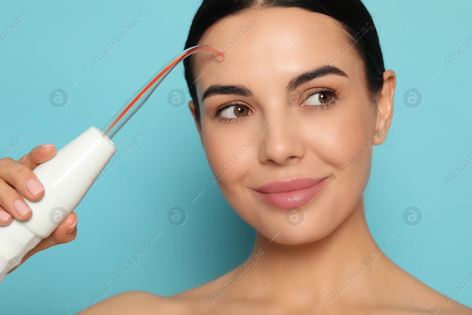 Photo of Woman using high frequency darsonval device on light blue background