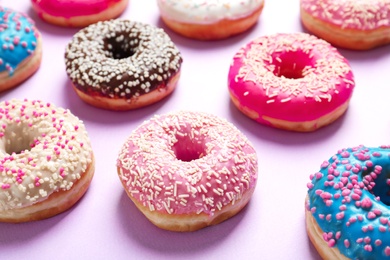 Delicious glazed doughnuts with sprinkles on color background