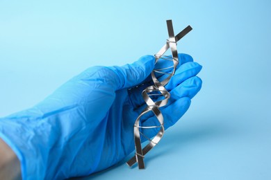 Photo of Scientist with DNA molecular chain model made of metal on light blue background, closeup