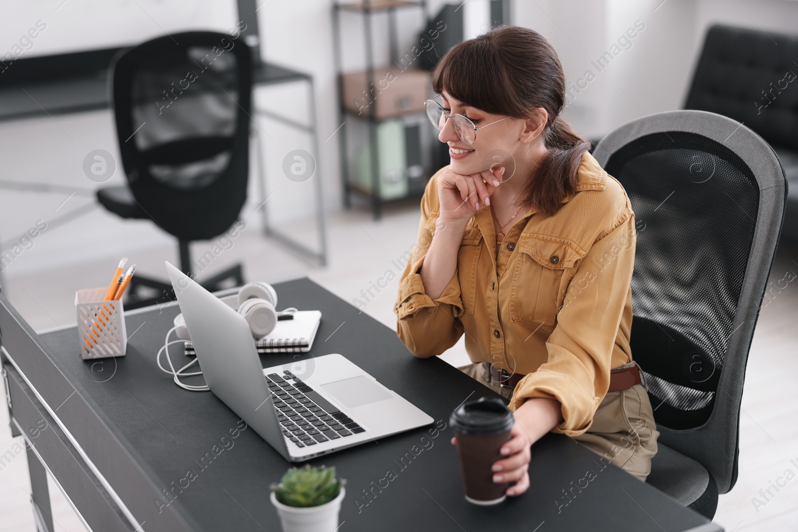 Photo of Woman with cup of coffee watching webinar at table in office