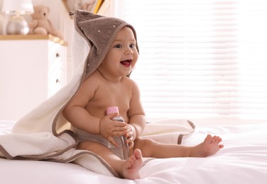 Cute little baby with towel and bottle of massage oil on bed at home