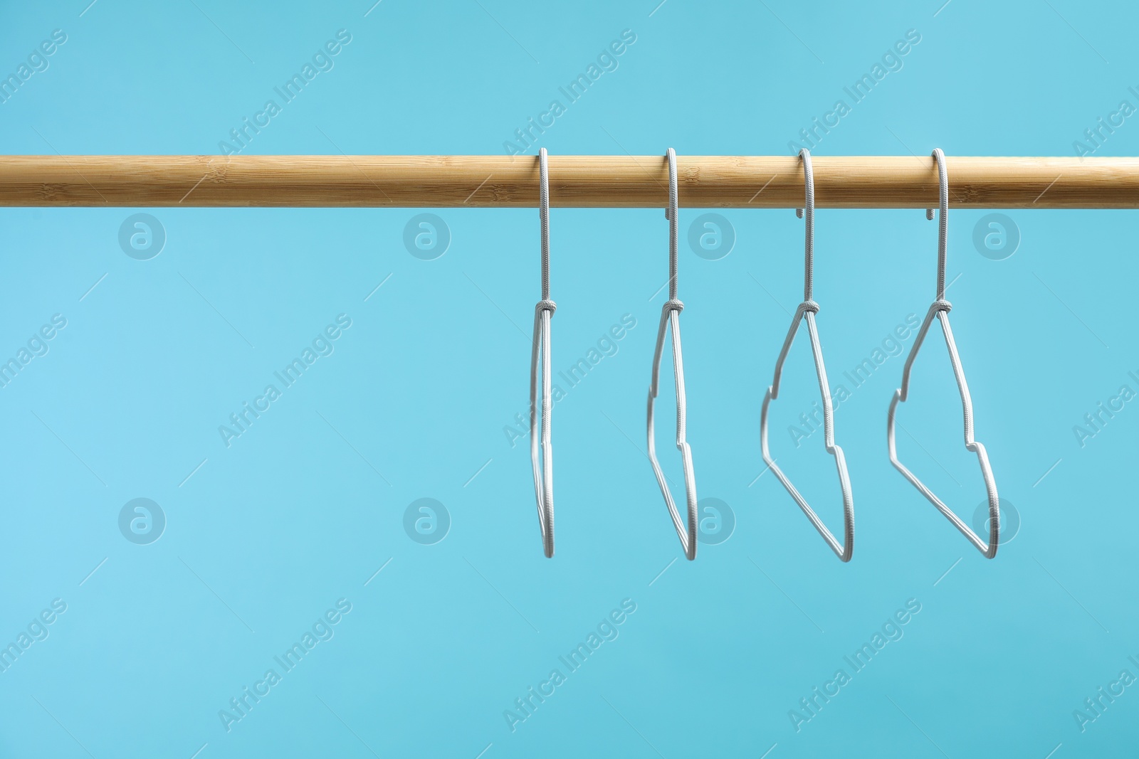 Photo of Empty clothes hangers on wooden rack against light blue background. Space for text