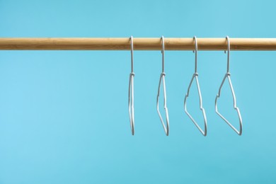 Photo of Empty clothes hangers on wooden rack against light blue background. Space for text