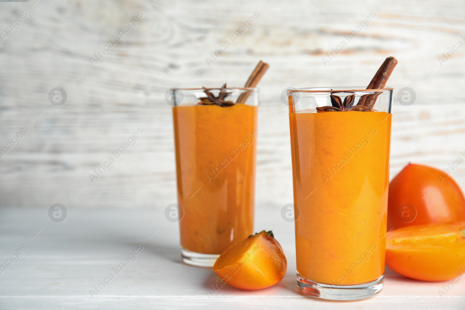 Photo of Tasty persimmon smoothie with anise and cinnamon on white wooden table. Space for text