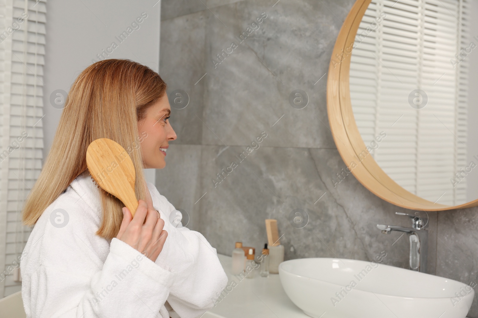 Photo of Beautiful woman brushing her hair near mirror in bathroom