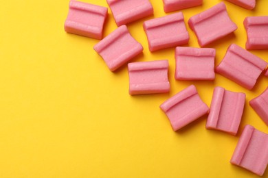 Photo of Tasty pink chewing gums on yellow background, flat lay. Space for text